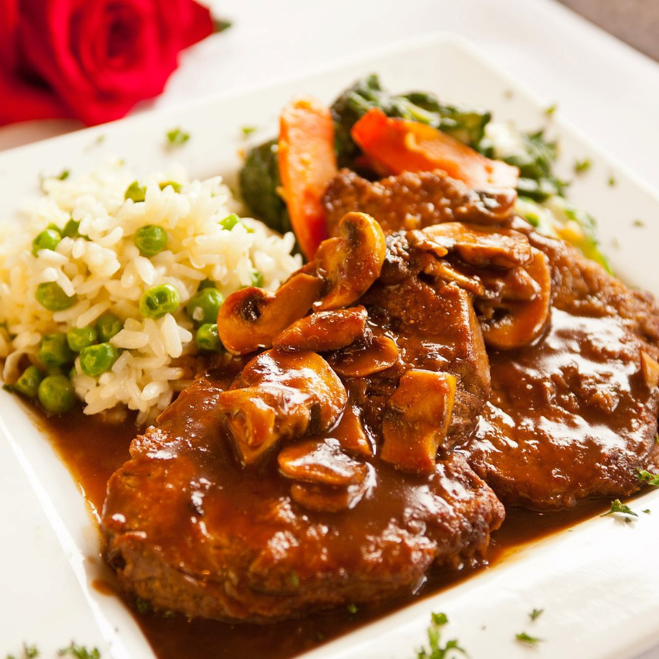 Veal Marsala with mushrooms, rice and peas, and vegetables, with a red rose in the background.