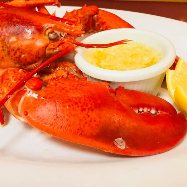 A bright red cooked lobster with a side of melted butter and a lemon wedge.